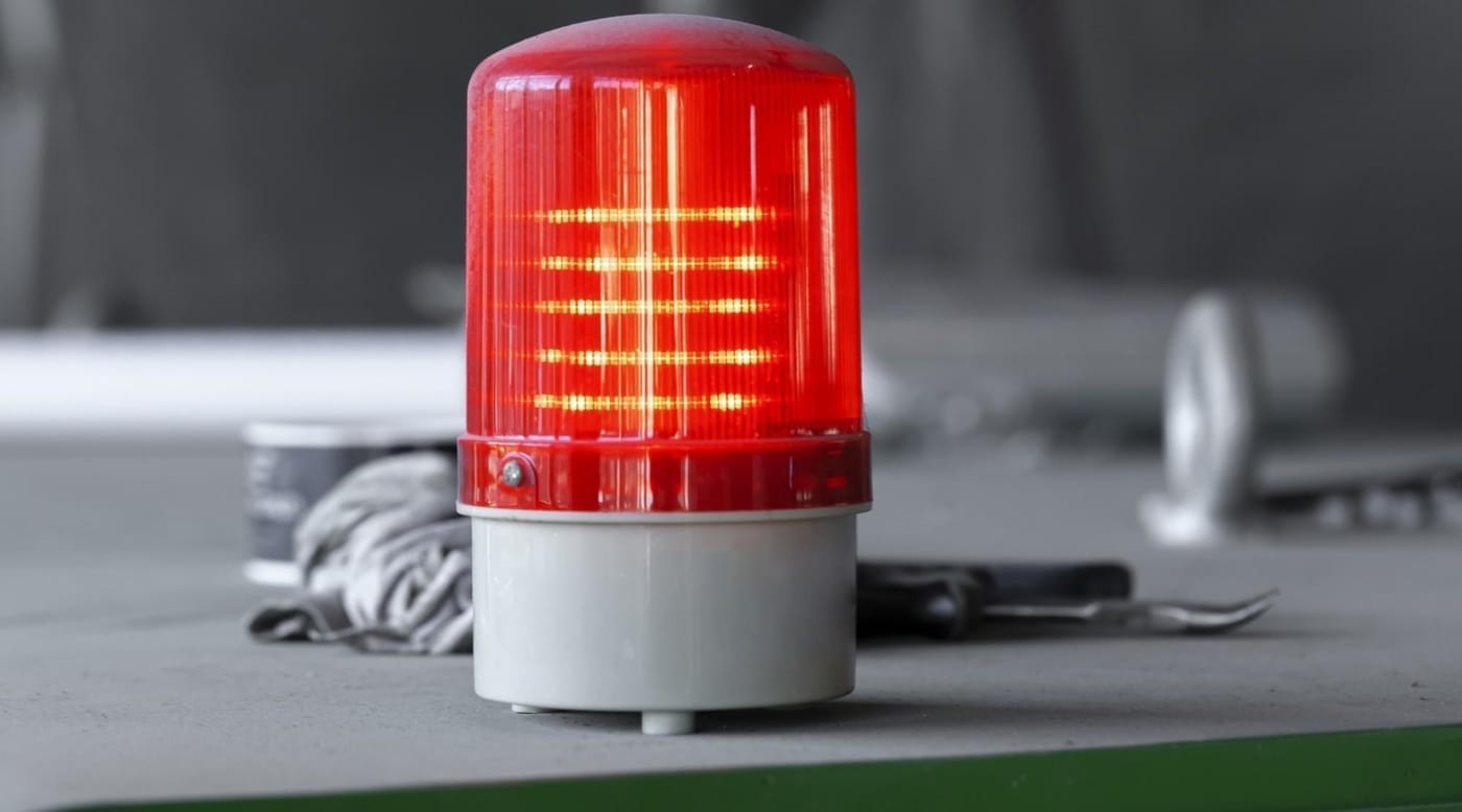 Photo of a red warning light in the foreground of a grey nondescript background.