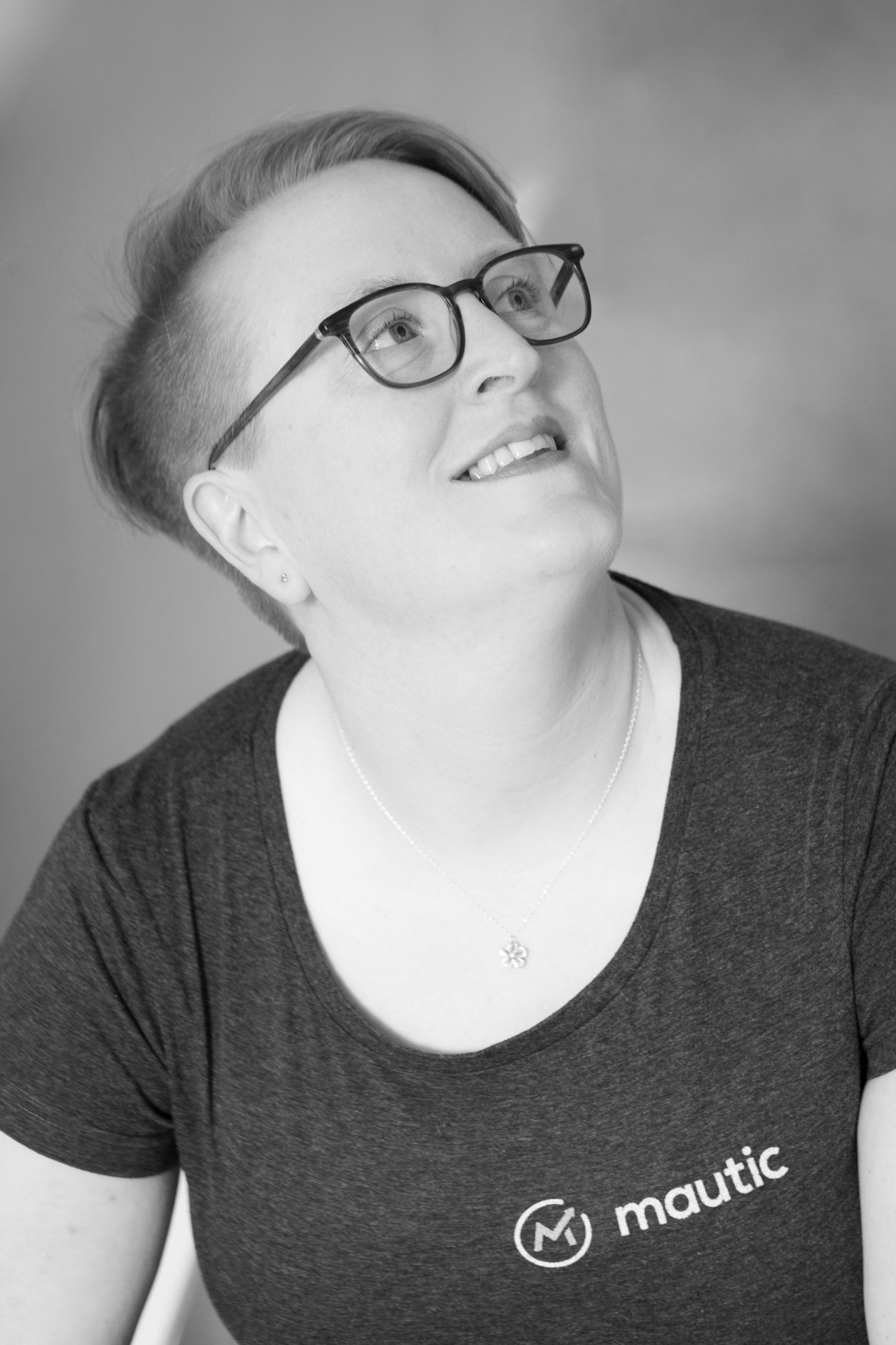 Black and white photo of Sīlavāpi in a Mautic T-shirt, looking upward and smiling.