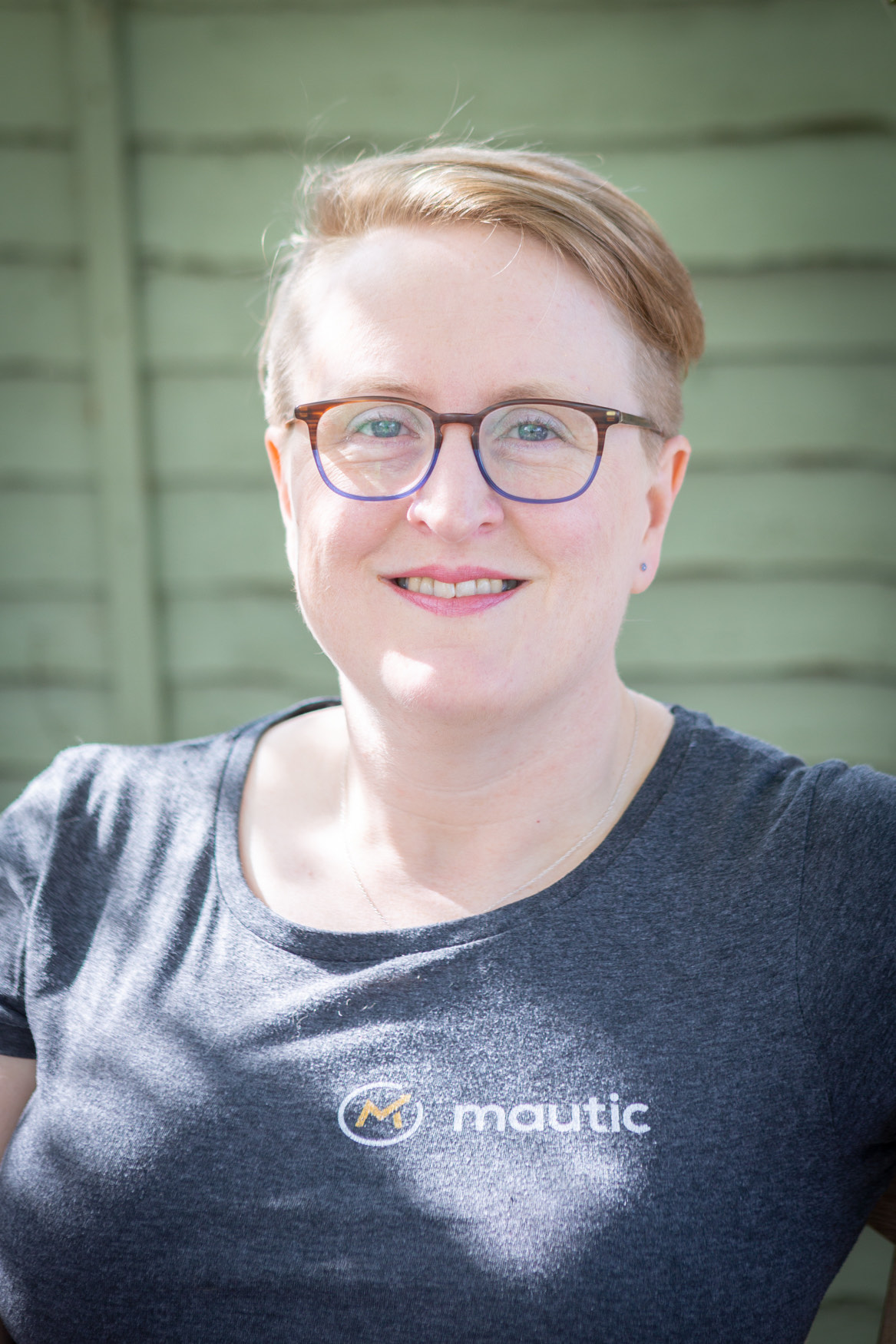 Sīlavāpi outdoors against a green fence, wearing a Mautic T-shirt and smiling to camera.