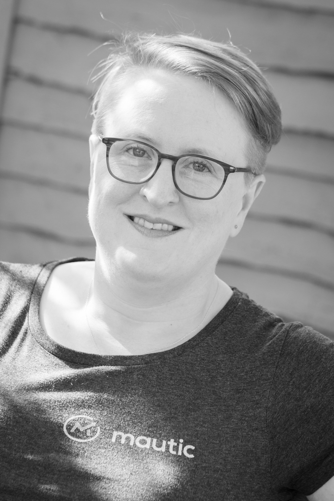 Black and white photo of Sīlavāpi outdoors in a Mautic T-shirt, smiling to camera.