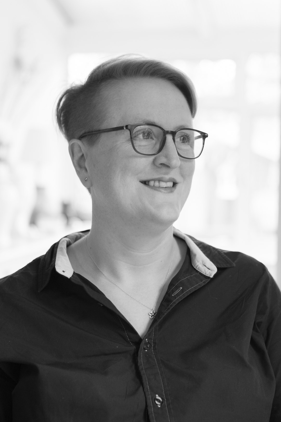 Black and white portrait of Sīlavāpi in profile, smiling, wearing a dark shirt with a white collar.