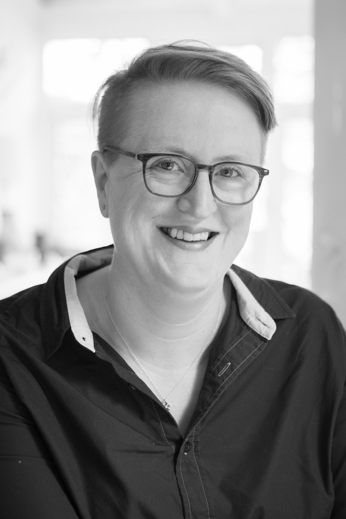 Black and white portrait of Sīlavāpi smiling to camera, in a dark shirt with a white collar.