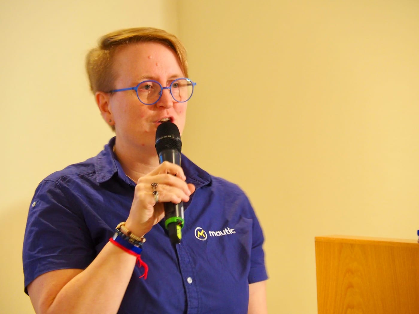 Sīlavāpi speaking into a handheld microphone, wearing a blue Mautic shirt.